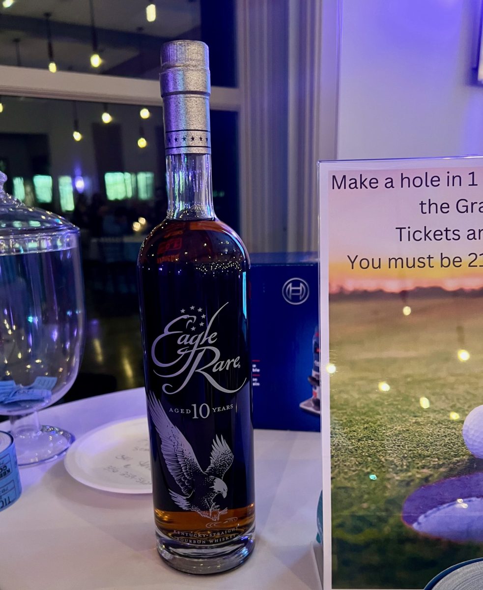 A bottle of Eagle Rare 10-year-old bourbon sits on a table beside a glass jar and part of a golf-themed sign.
